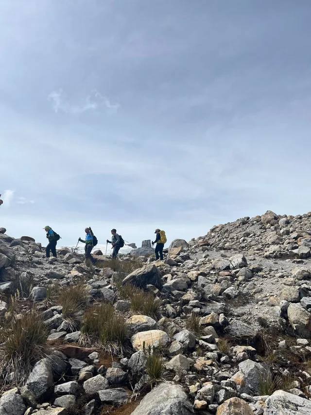 A group walking in single file across the moraine of El Cocuy National Natural Park, with the Púlpito del Diablo behind