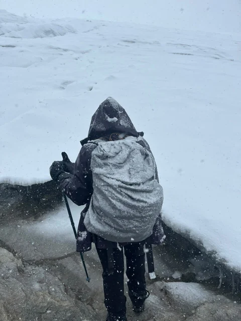 A hiker climbing Ritacuba with a snow-covered pack, during a snowfall