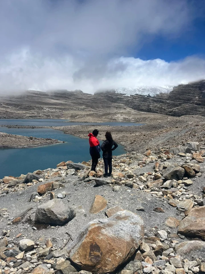 Two hikers in front of the lakes at Laguna Grande de la Sierra, with the glacier among the clouds behind
